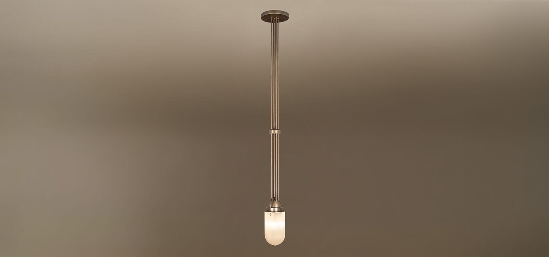 Russell Pendant Lamp The Russell pendant lamp by Porus Studio, featuring an elegant industrial design crafted from brushed brass and alabaster. A cluster of long, slender brushed brass rods extends vertically from a circular ceiling canopy to a luminous, dome-shaped alabaster diffuser. A matching brass ring accents the central rods, highlighting the lamp's refined architectural silhouette against a neutral gradient background.