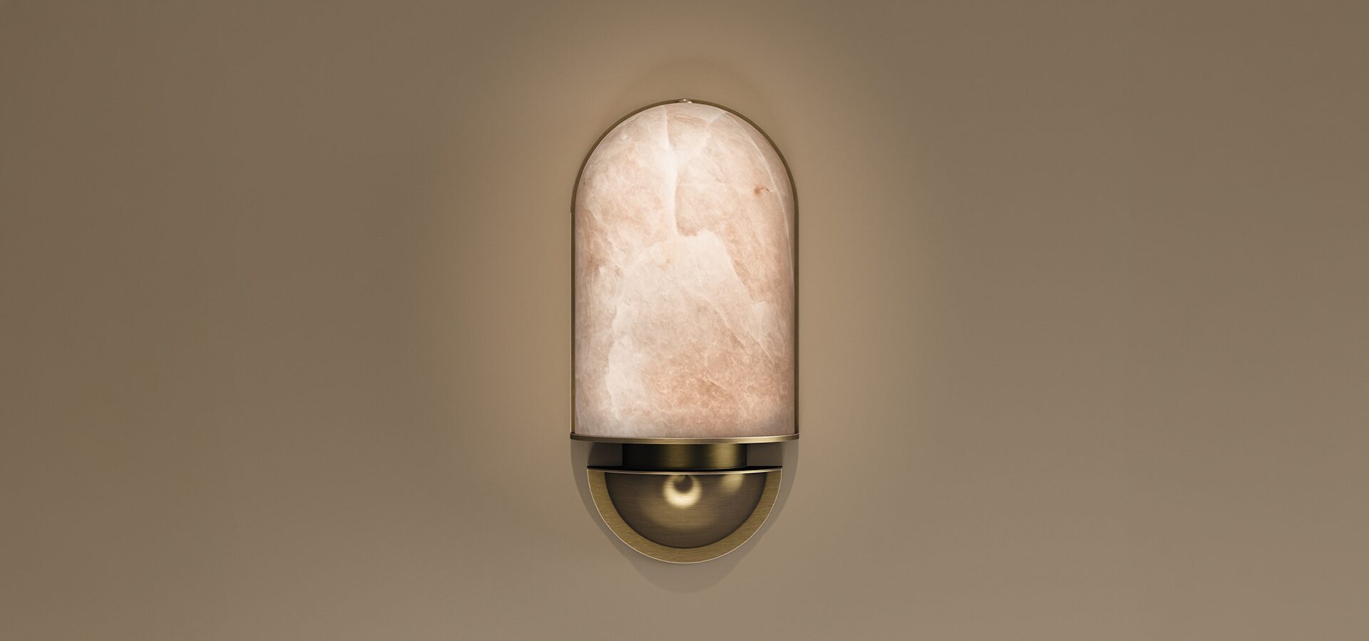 A vertical wall sconce, the Russell I Wall Lamp by Porus Studio, featuring a minimalist dome-shaped lampshade made of translucent alabaster with natural veining. The stone shade sits atop a sleek, brushed brass base with a concave semi-circular detail, mounted against a neutral beige wall.