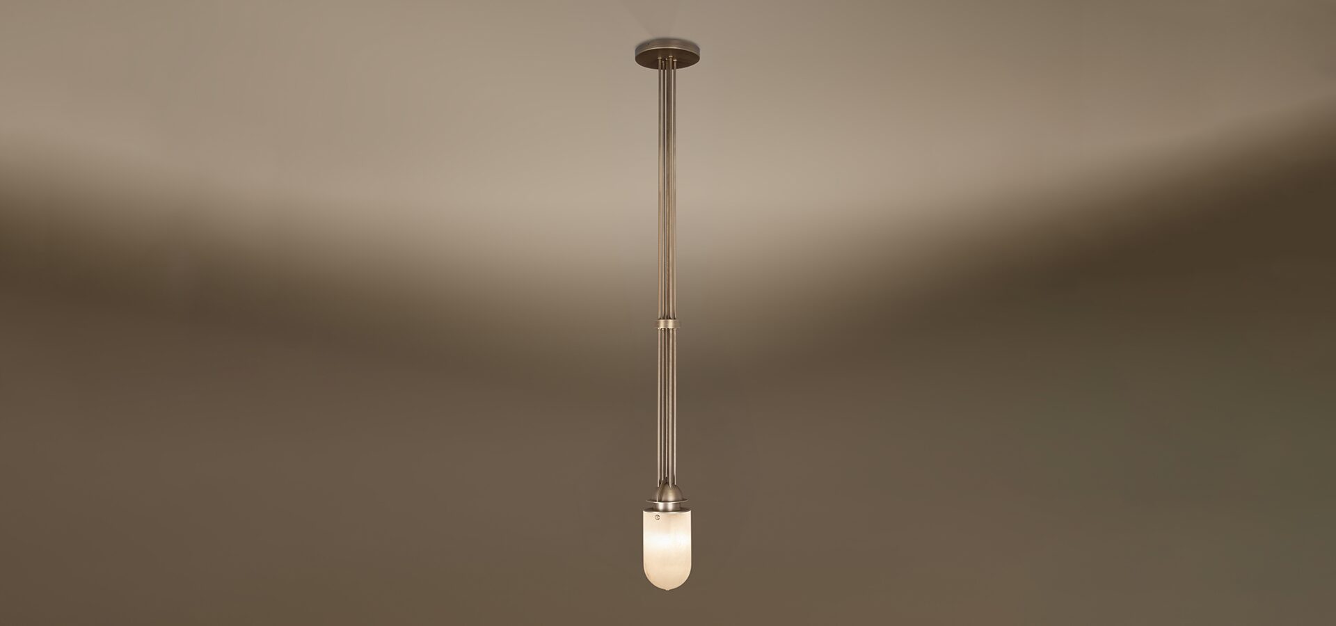 The Russell pendant lamp by Porus Studio, featuring an elegant industrial design crafted from brushed brass and alabaster. A cluster of long, slender brushed brass rods extends vertically from a circular ceiling canopy to a luminous, dome-shaped alabaster diffuser. A matching brass ring accents the central rods, highlighting the lamp's refined architectural silhouette against a neutral gradient background.