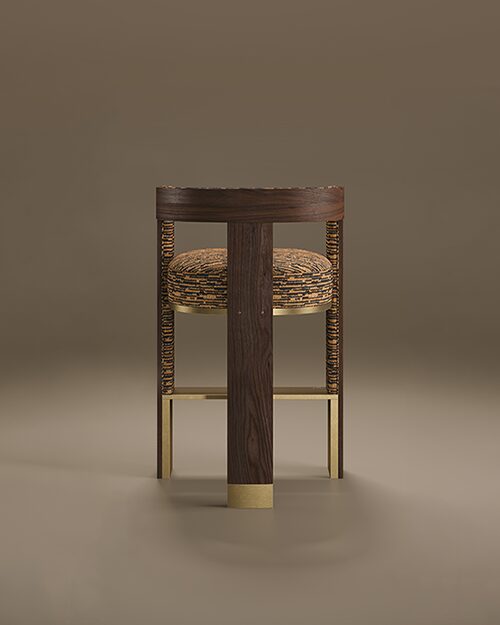 A rear-view studio shot of the Brooklyn Bar Chair by Porus Studio, a modern furniture piece inspired by the iconic architecture of the Brooklyn Bridge. The chair features a prominent, vertical central spine made of dark walnut wood with a rich grain, accented at the base with a brushed brass cuff. This wooden structure supports a curved backrest and a thick, rounded seat upholstered in a textured orange and black patterned fabric. The side supports and horizontal footrest are crafted from polished brass, creating a geometric, industrial-chic silhouette. The chair is set against a neutral, warm taupe background with soft reflections on the floor.