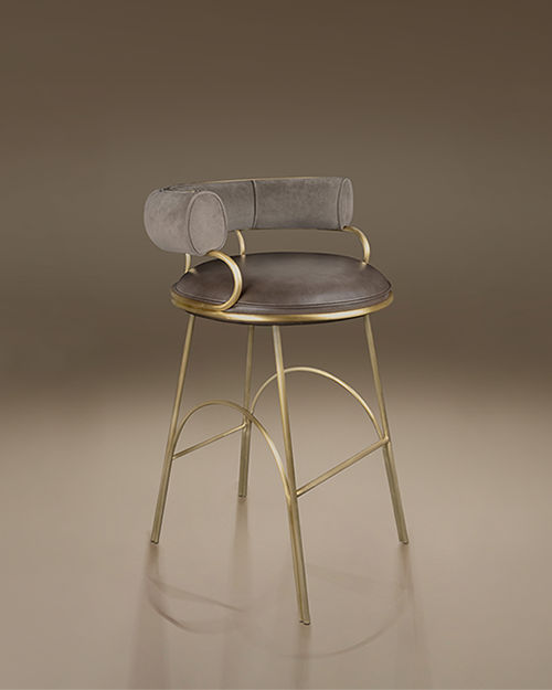 A contemporary bar chair (Austin Bar Chair by Porus Studio) with a distinct Art Deco flair, set against a smooth, warm taupe studio background. The chair features a striking metal frame made of polished, warm brass-finished steel, with slender legs and arched supports that serve as footrests.
