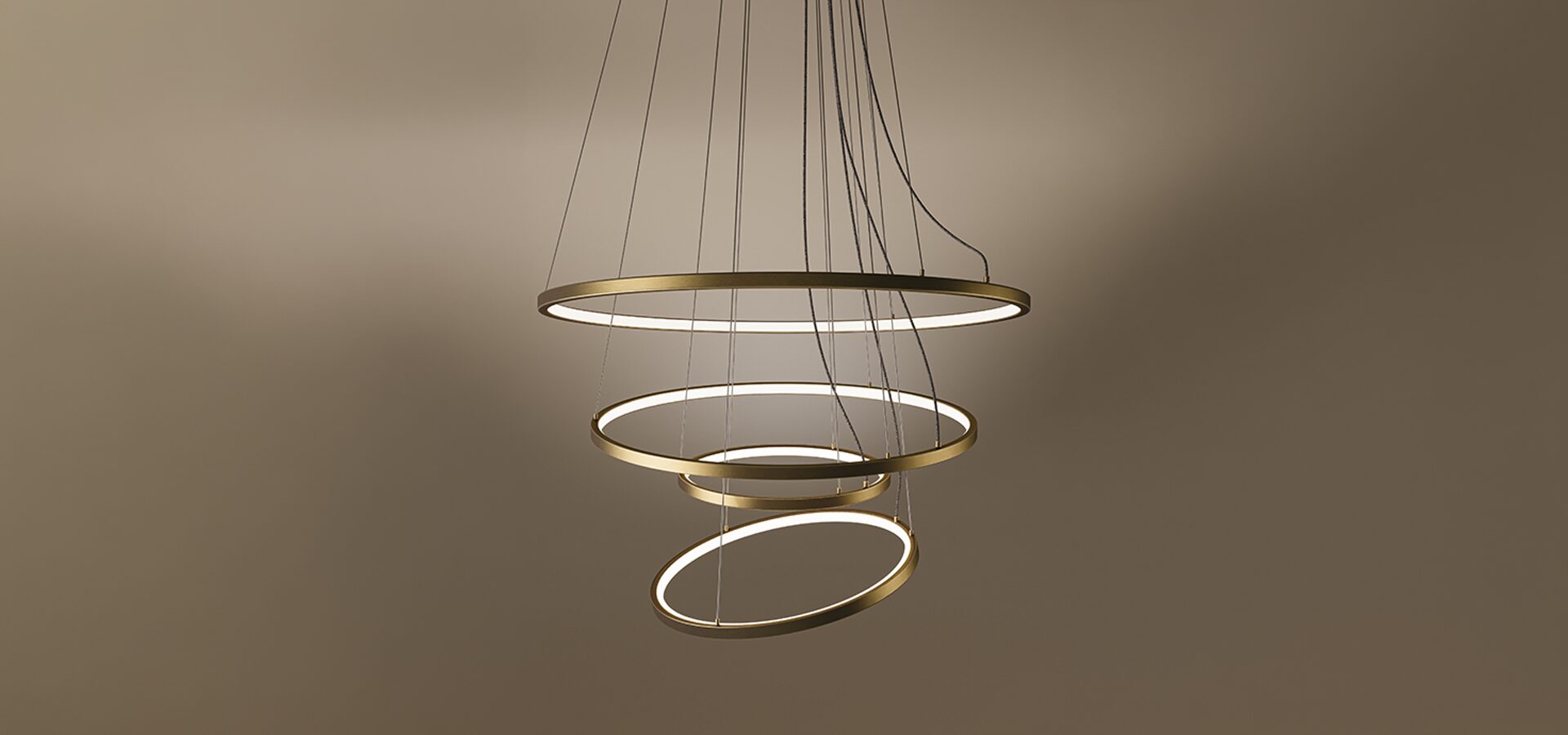 The Gateway suspension lamp, a modern multi-tier LED chandelier featuring four concentric rings with a sleek brass finish. Each ring is suspended by delicate cables, creating a dynamic, spiraling form. The interior of the rings emits a clean, warm light against a dark brown gradient background, showcasing a contemporary and architectural design.