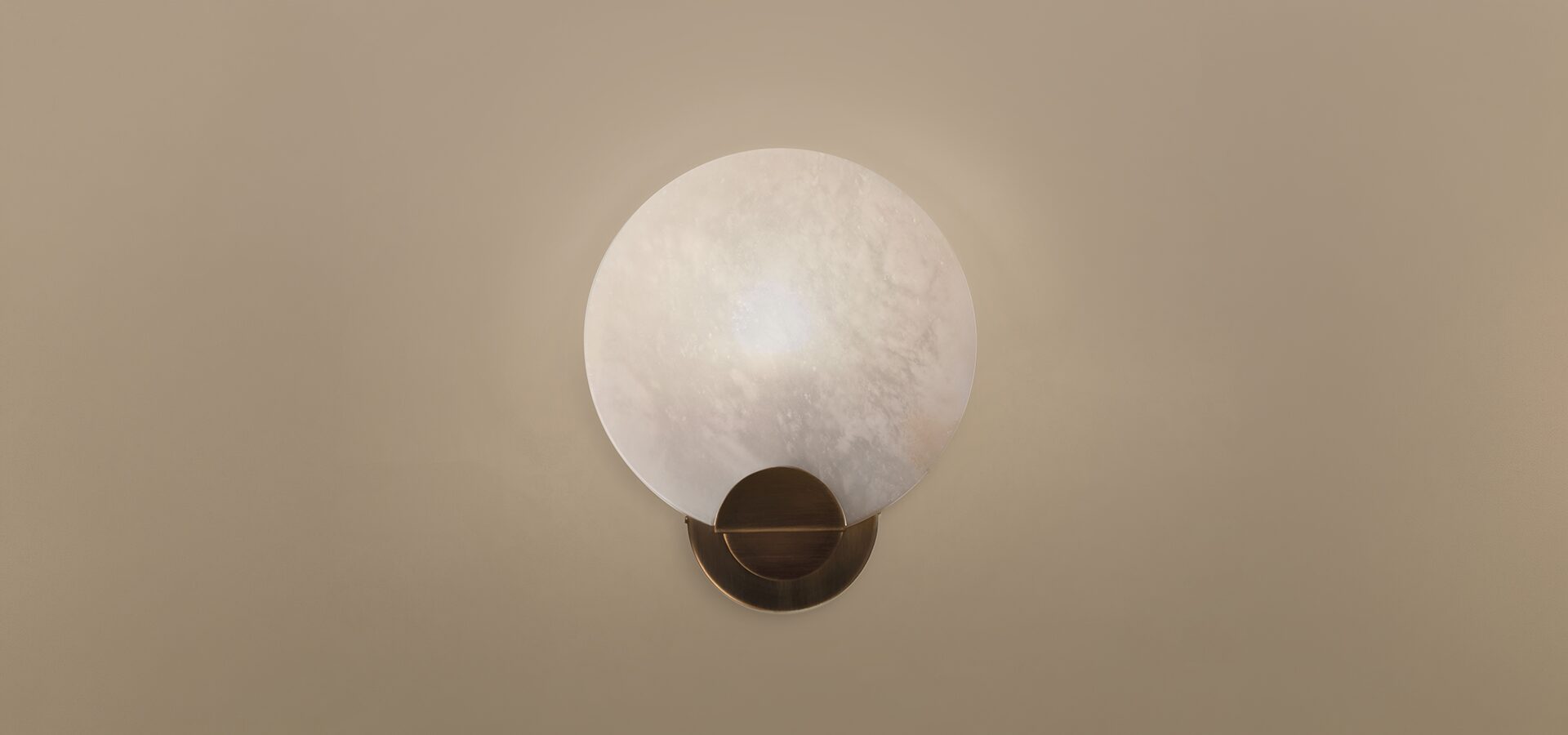 Walla Walla Wall Lamp Walla Walla Wall Lamp by Porus Studio, featuring a circular alabaster lampshade and aged brushed brass details against a neutral wall.