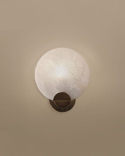 Walla Walla Wall Lamp by Porus Studio, featuring a circular alabaster lampshade and aged brushed brass details against a neutral wall.