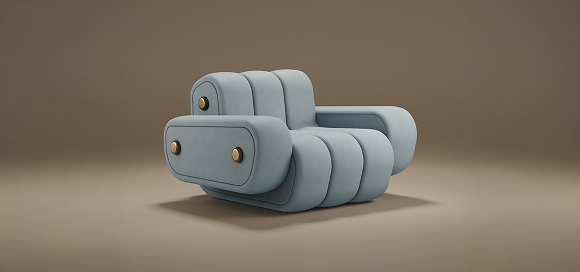 A professional studio shot of the Dakota Armchair by Porus Studio, presented against a soft, neutral brown background. The armchair features a bold, modular aesthetic with a low-profile silhouette. It is fully upholstered in a smooth, pale blue-grey velvet, characterized by thick, vertical channeled tufting that creates a rounded, "puffy" appearance. The wide, blocky armrests and the backrest are embellished with distinctive brushed brass circular studs, adding a touch of industrial luxury to the soft design. The chair sits on a recessed base, giving it a heavy, grounded, yet contemporary feel.