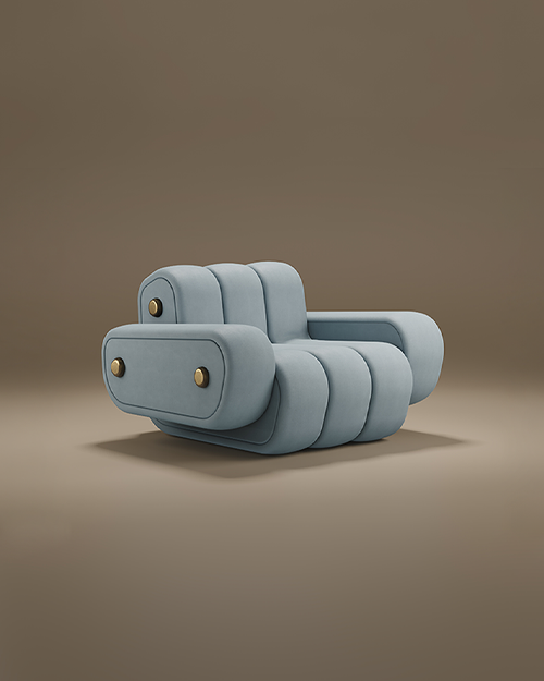 A professional studio shot of the Dakota Armchair by Porus Studio, presented against a soft, neutral brown background. The armchair features a bold, modular aesthetic with a low-profile silhouette. It is fully upholstered in a smooth, pale blue-grey velvet, characterized by thick, vertical channeled tufting that creates a rounded, "puffy" appearance. The wide, blocky armrests and the backrest are embellished with distinctive brushed brass circular studs, adding a touch of industrial luxury to the soft design. The chair sits on a recessed base, giving it a heavy, grounded, yet contemporary feel.