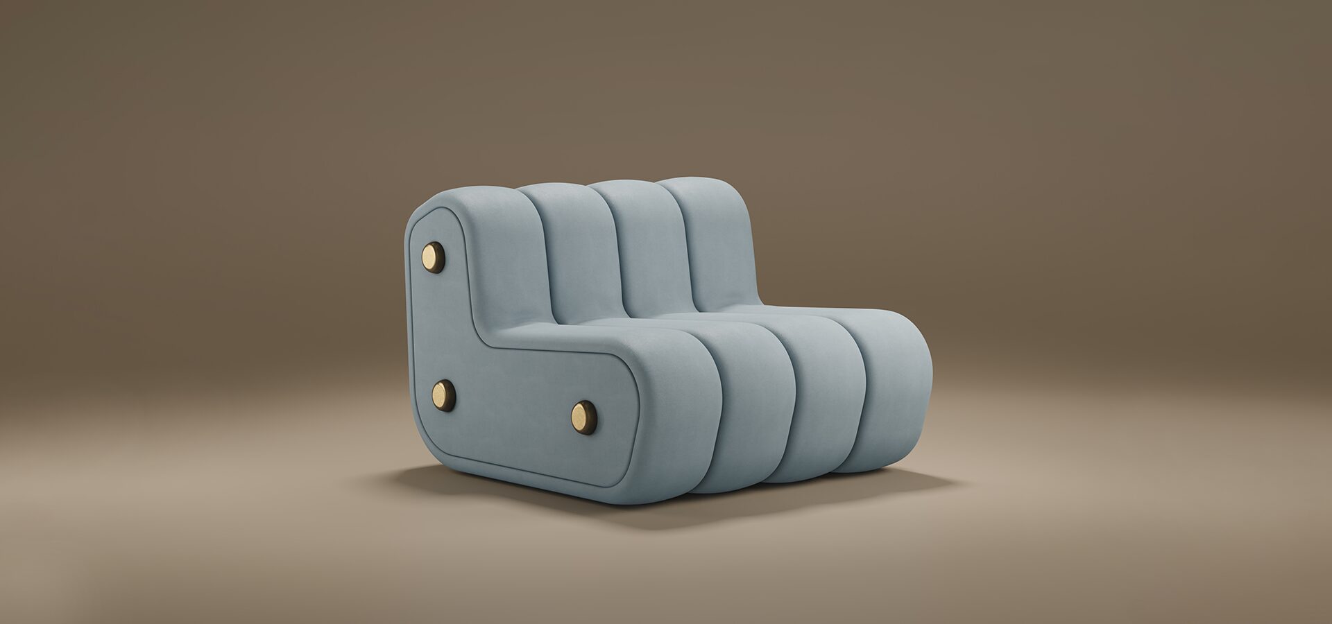A studio product shot of the Dakota Lounge Chair by Porus Studio, showcased against a muted, warm brown background. The lounge chair features an armless, low-slung modular design with a soft, sculptural presence. It is fully upholstered in a pale blue-grey velvet and defined by bold, vertical channeled tufting that gives it a rounded, segmented look. The side profile reveals an L-shaped silhouette adorned with three decorative brushed brass circular studs, providing a luxurious metallic accent to the matte fabric. Its seamless, floor-length base emphasizes a heavy, grounded, and contemporary aesthetic.