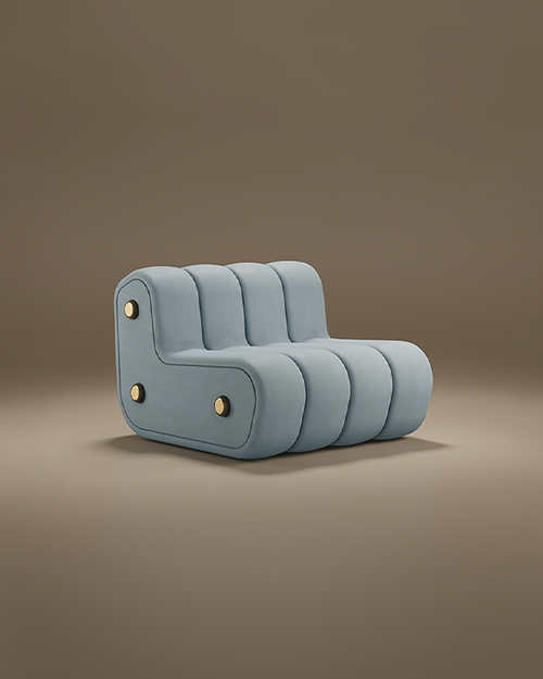 A studio product shot of the Dakota Lounge Chair by Porus Studio, showcased against a muted, warm brown background. The lounge chair features an armless, low-slung modular design with a soft, sculptural presence. It is fully upholstered in a pale blue-grey velvet and defined by bold, vertical channeled tufting that gives it a rounded, segmented look. The side profile reveals an L-shaped silhouette adorned with three decorative brushed brass circular studs, providing a luxurious metallic accent to the matte fabric. Its seamless, floor-length base emphasizes a heavy, grounded, and contemporary aesthetic.