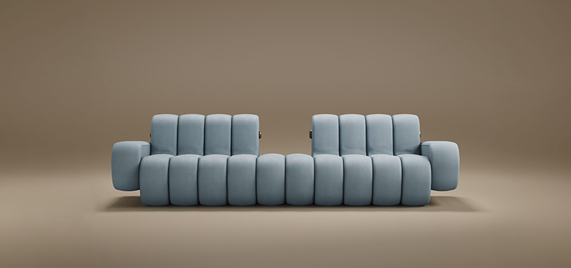 A contemporary Dakota Sofa featuring thick, vertical padded sections. Upholstered in a soft powder-blue fabric, the sofa boasts a unique silhouette with two separate backrests and integrated low-profile armrests. Small brass metallic accents are visible on the sides, adding a touch of luxury. The piece is set against a seamless, warm taupe background.