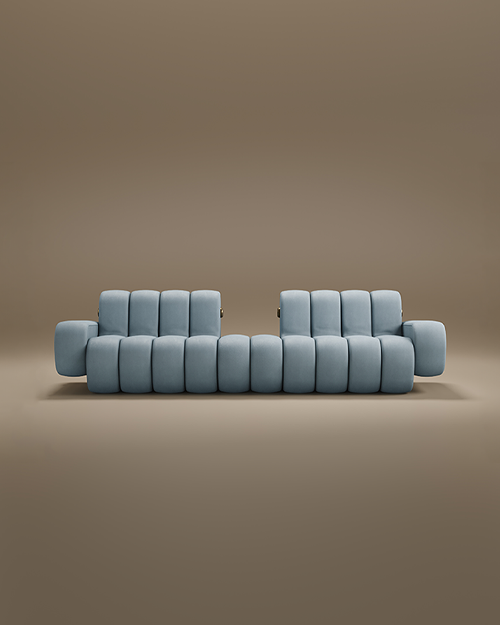 A contemporary Dakota Sofa featuring thick, vertical padded sections. Upholstered in a soft powder-blue fabric, the sofa boasts a unique silhouette with two separate backrests and integrated low-profile armrests. Small brass metallic accents are visible on the sides, adding a touch of luxury. The piece is set against a seamless, warm taupe background.