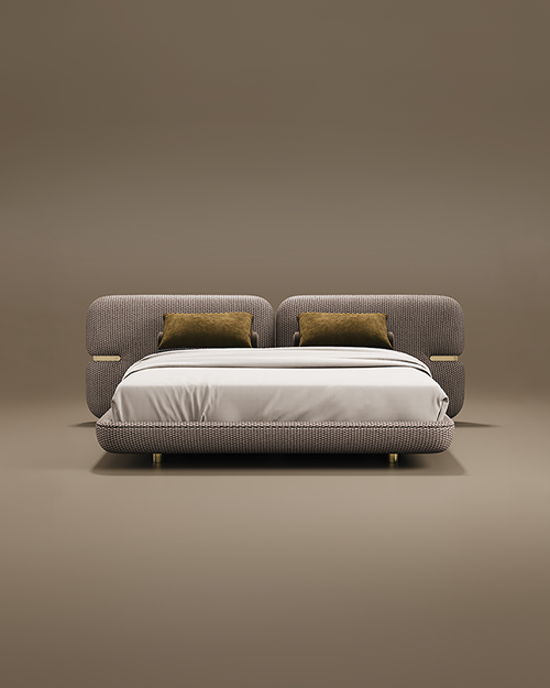 A contemporary Newark Bed featuring a wide headboard and frame upholstered in a textured, woven fabric. The headboard is split into two large rounded panels, each accented with a polished brass inset detail on the outer sides. Two mustard-yellow velvet cushions lean against the headboard, contrasting with the neutral white bedding. The bed is supported by small, cylindrical brass feet and set against a warm taupe background.