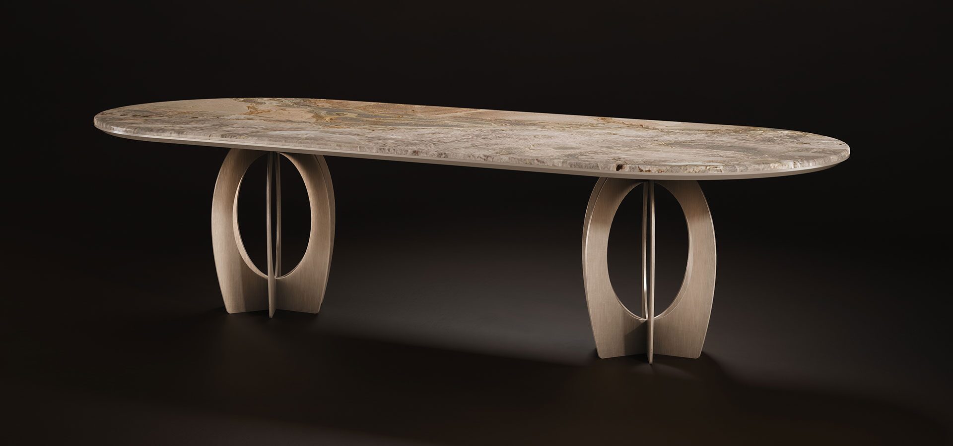 Boulder Oval Dining Table A luxurious Boulder Oval Dining Table by Porus Studio, featuring a long, oval-shaped top made of polished natural marble with rich, earthy veining. The table is supported by two architectural brushed-metal bases with a distinctive open-circle, interlaced design, set against a dark background."