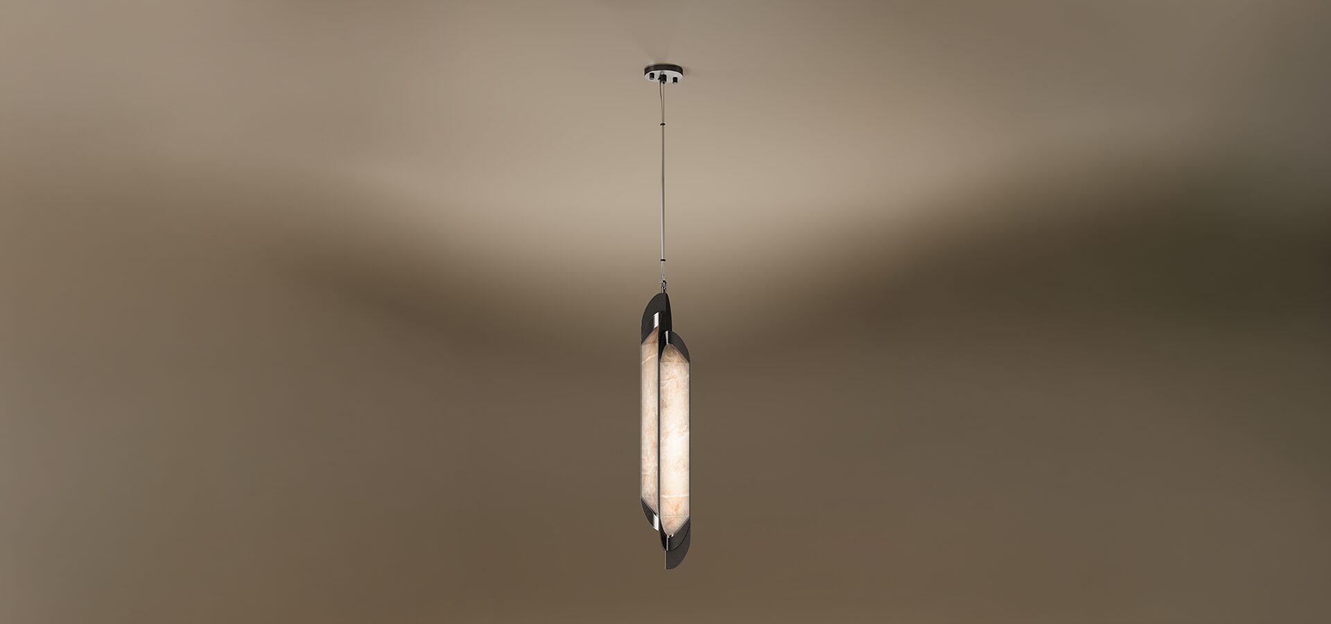 A vertical Glacier I pendant lamp by Porus Studio, featuring a slender, elongated design. A glowing center made of textured, warm-toned alabaster is held between two dark, curved metallic plates that overlap slightly. The fixture is suspended from a single thin cable set against a soft, neutral gradient background.