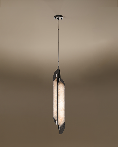 A vertical Glacier I pendant lamp by Porus Studio, featuring a slender, elongated design. A glowing center made of textured, warm-toned alabaster is held between two dark, curved metallic plates that overlap slightly. The fixture is suspended from a single thin cable set against a soft, neutral gradient background.