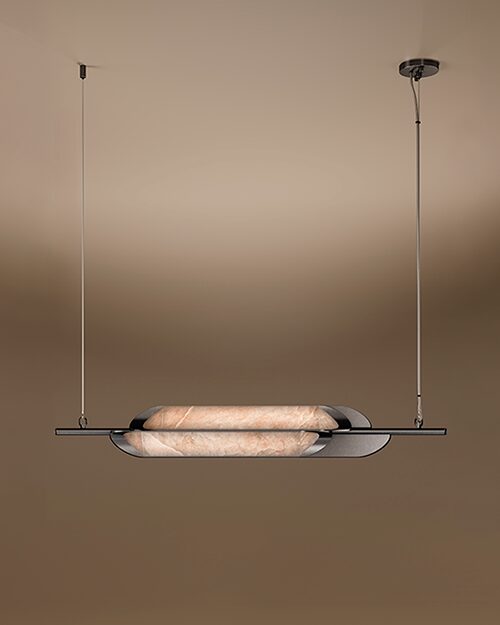 A horizontal Glacier II pendant lamp by Porus Studio, featuring a sleek, minimalist design. A luminous, capsule-shaped center made of textured alabaster is cradled by dark, curved metallic plates. The fixture is suspended from the ceiling by two thin vertical cables against a warm, neutral gradient background.
