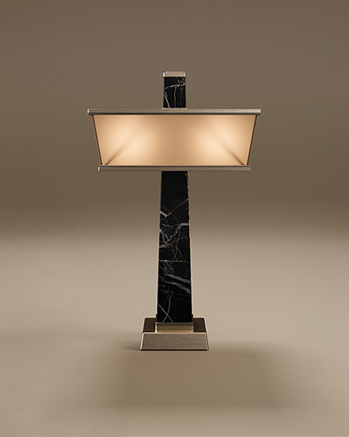 Liberty Table Lamp by Porus Studio. An architectural table lamp inspired by the Statue of Liberty's torch, featuring a tall, tapering obelisk structure made of marble. The design is complemented by a wide, rectangular shade and accents crafted in brushed stainless steel, including a sturdy square base. The lamp features a frosted glass diffuser that emits a warm glow, presented against a minimal taupe background.