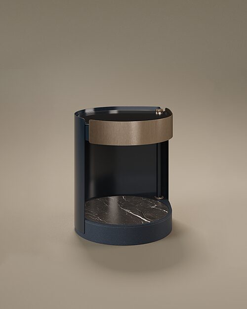 A luxury Rockefeller Bedside Table by Porus Studio featuring a cylindrical, open-front design. The outer frame is finished in dark blue matte lacquer, while the upper drawer section is highlighted by a wide band of aged brushed brass. The interior features a lower shelf made of marble with prominent white and gold veins, and the top is finished with black glass. The base is subtly wrapped in dark leather, all set against a neutral taupe studio background.