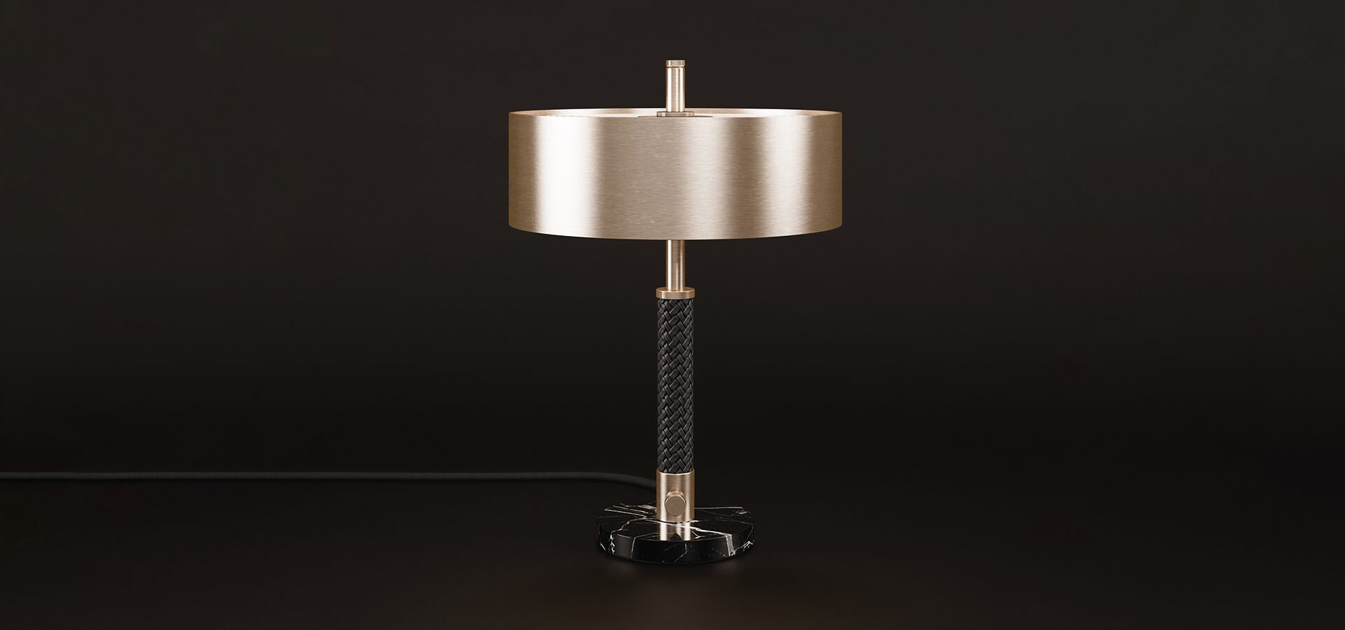 Front view of the Chicago table lamp set against a dark brown background, where cool stainless steel and solid marble are balanced by a central braided leather element, creating a tactile contrast between cold metal and warm artisanal texture.
