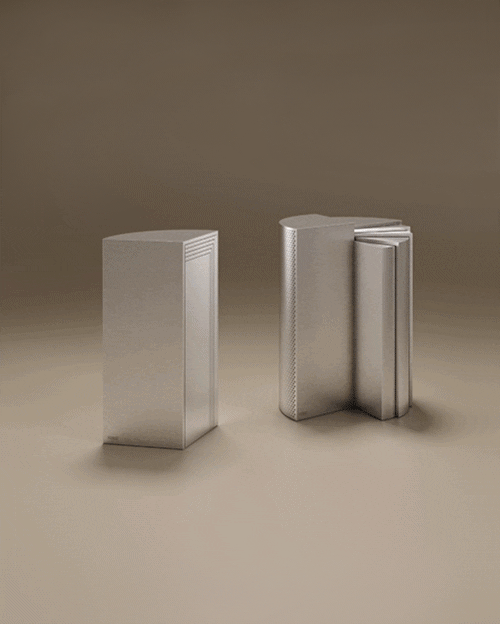 A luxury Seagram Side Table set by Porus Studio, featuring two modular, wedge-shaped units with an architectural design. The pieces are finished in a silver metal, with one unit showing a smooth face and the other displaying a decorative vertical fluted pattern. The metallic, monolithic tables are inspired by skyscraper architecture and are set against a warm, neutral studio background.