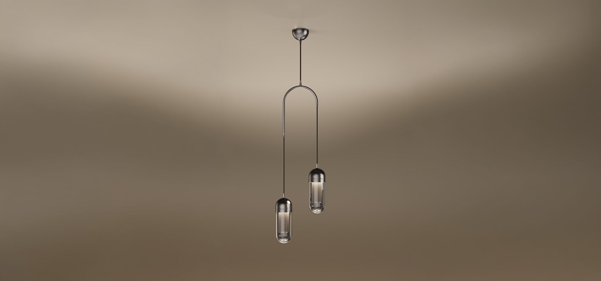 The Denver II pendant lamp by Porus Studio, featuring two sophisticated capsule-shaped light fixtures suspended at different heights from a dark metallic arch. Each fixture has a dark metal cap and a transparent glass diffuser enclosing a glowing internal mesh cylinder. A single central cable connects the arch to a dark metal ceiling canopy. The entire lamp is set against a soft, warm-toned studio background.