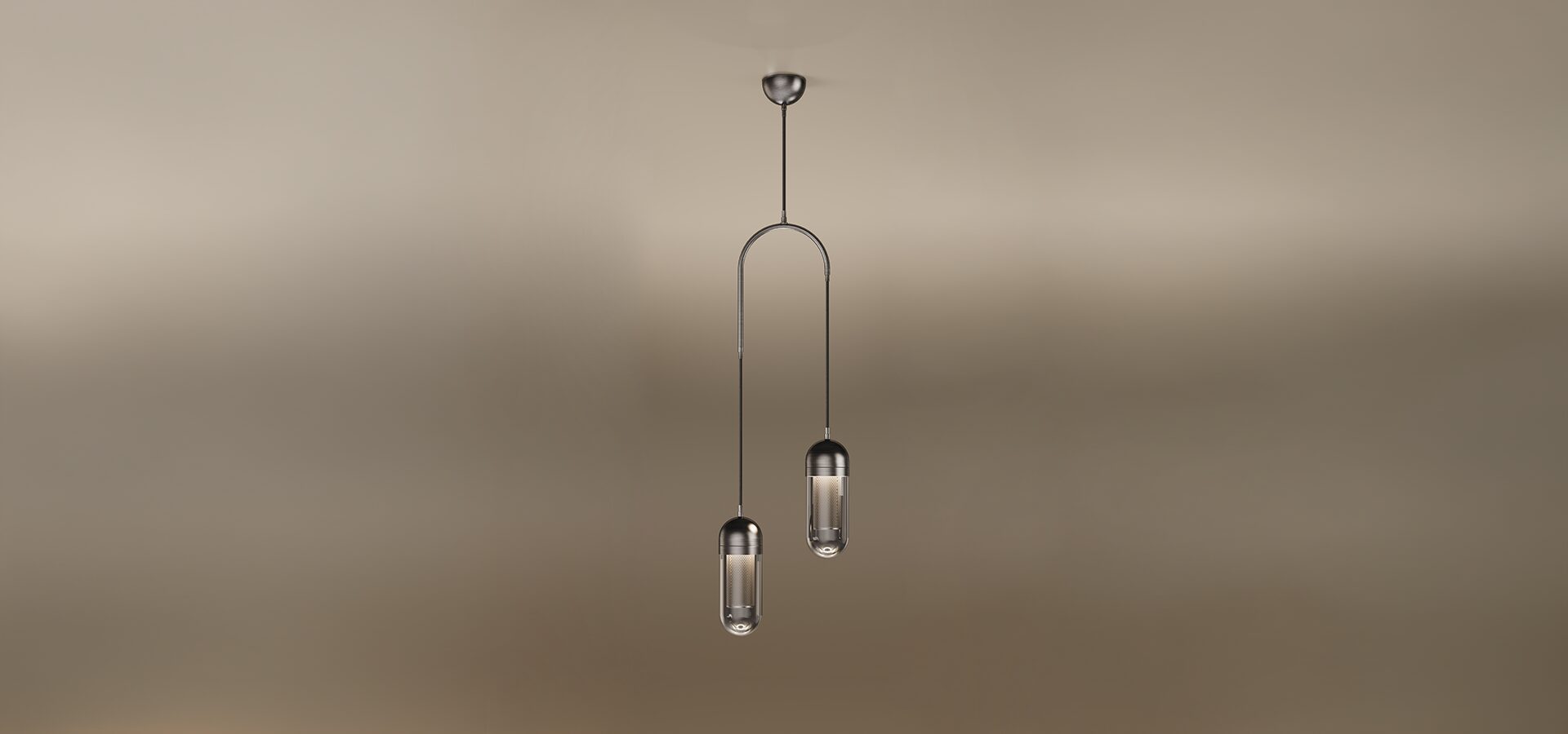The Denver II pendant lamp by Porus Studio, featuring two sophisticated capsule-shaped light fixtures suspended at different heights from a dark metallic arch. Each fixture has a dark metal cap and a transparent glass diffuser enclosing a glowing internal mesh cylinder. A single central cable connects the arch to a dark metal ceiling canopy. The entire lamp is set against a soft, warm-toned studio background.