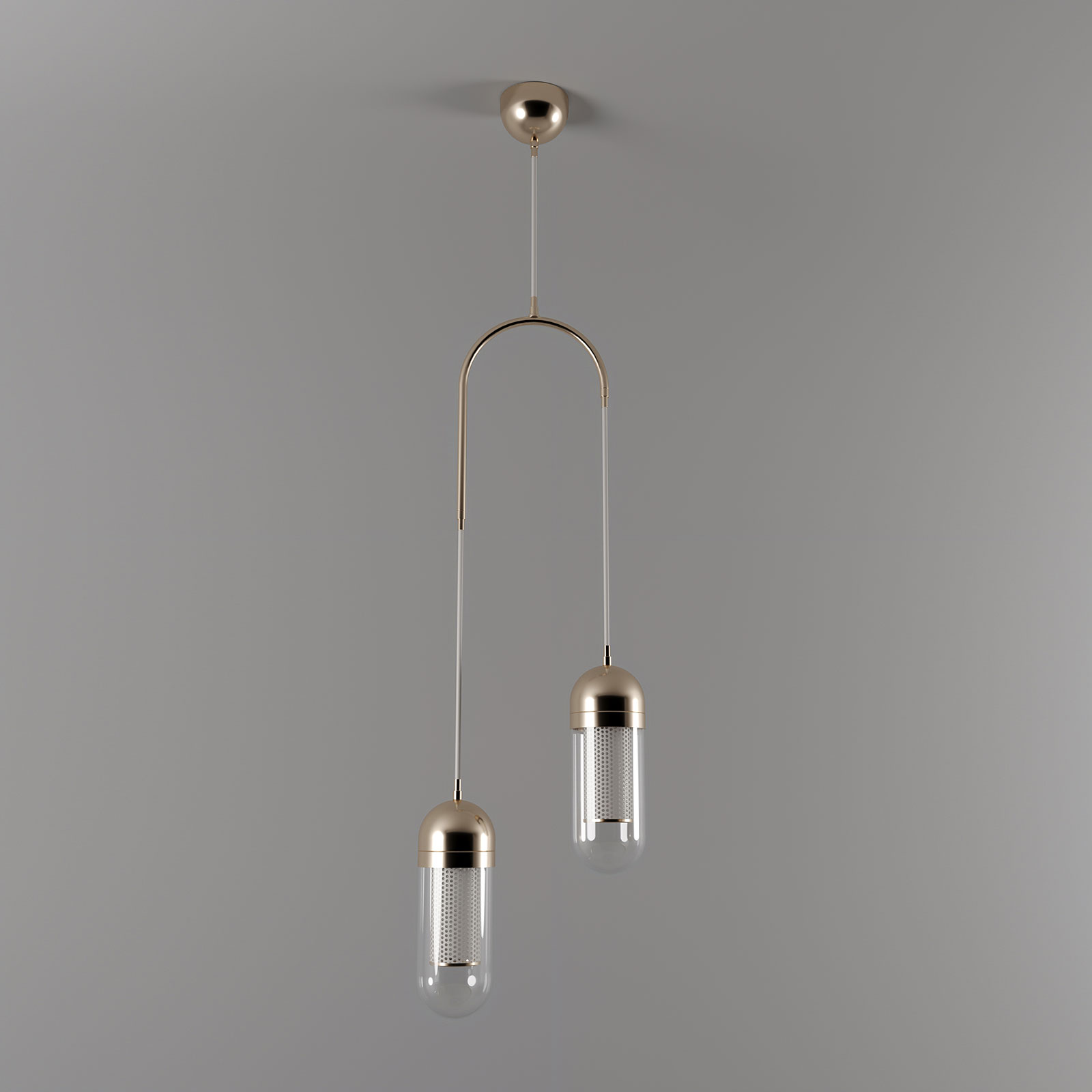 Denver II Pendant Lamp A professional studio photograph of the Denver II Pendant Lamp by Porus Studio, featuring a sophisticated asymmetric design suspended from a single ceiling mount against a dark grey background with the lights turned off. The structure is composed of a polished copper-toned stainless steel arch supporting two vertical cables of differing lengths. Each cable ends in a capsule-shaped fixture with a metallic top, a clear glass body, and an internal core of perforated white lacquered stainless steel, highlighting the refined craftsmanship, industrial precision, and contemporary luxurious aesthetic.