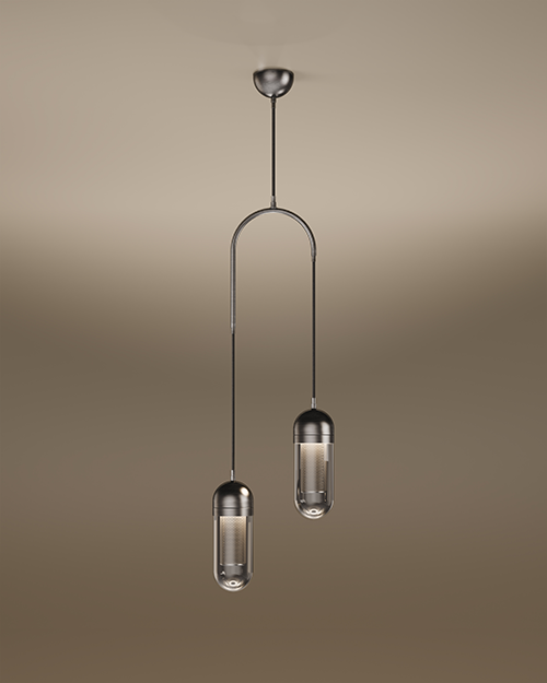 The Denver II pendant lamp by Porus Studio, featuring two sophisticated capsule-shaped light fixtures suspended at different heights from a dark metallic arch. Each fixture has a dark metal cap and a transparent glass diffuser enclosing a glowing internal mesh cylinder. A single central cable connects the arch to a dark metal ceiling canopy. The entire lamp is set against a soft, warm-toned studio background.