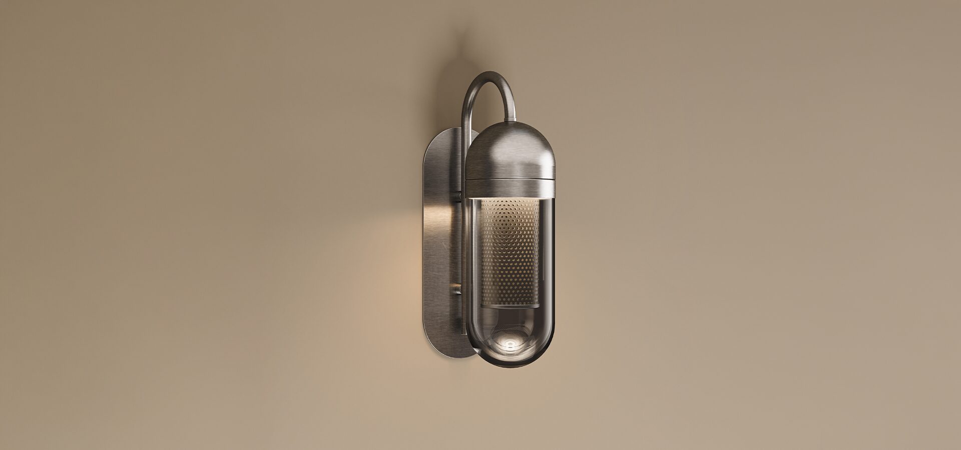 The Denver Wall Lamp by Porus Studio, featuring a stainless steel finish, a curved supporting arm, and a clear glass capsule-shaped shade with an internal perforated metal mesh diffuser.