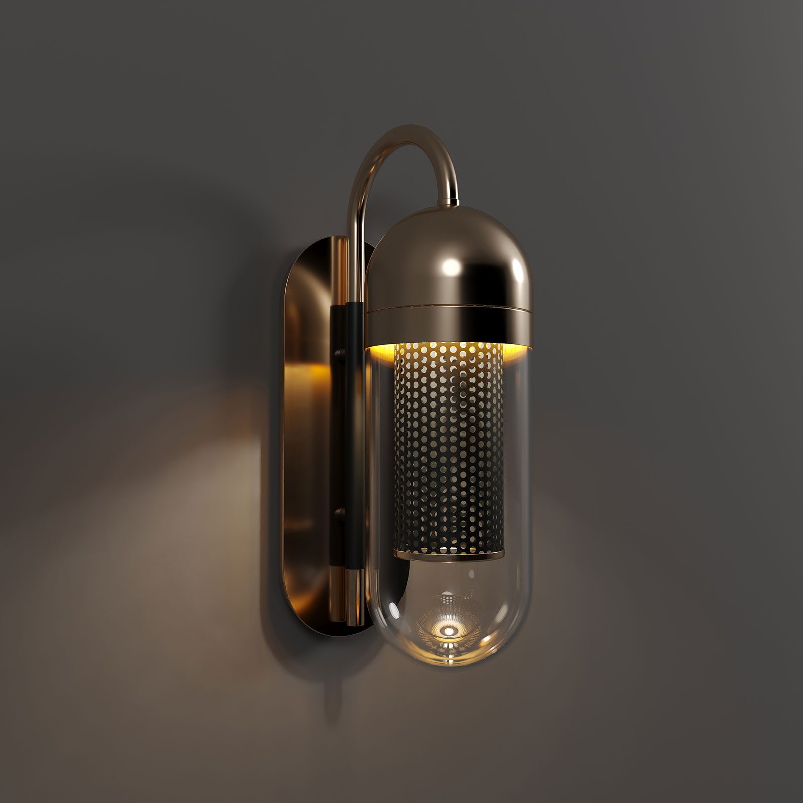 Denver Wall Lamp A luxury Denver Wall Lamp by Porus Studio, featuring a pill-shaped clear glass diffuser. The lamp is constructed with a curved polished brass arm and a mounting plate. Inside the glass, a lacquered perforated stainless steel cylinder houses the light source, emitting a warm, diffused glow through the small circular cutouts. The lamp is mounted on a dark charcoal wall, casting a soft, atmospheric amber light.