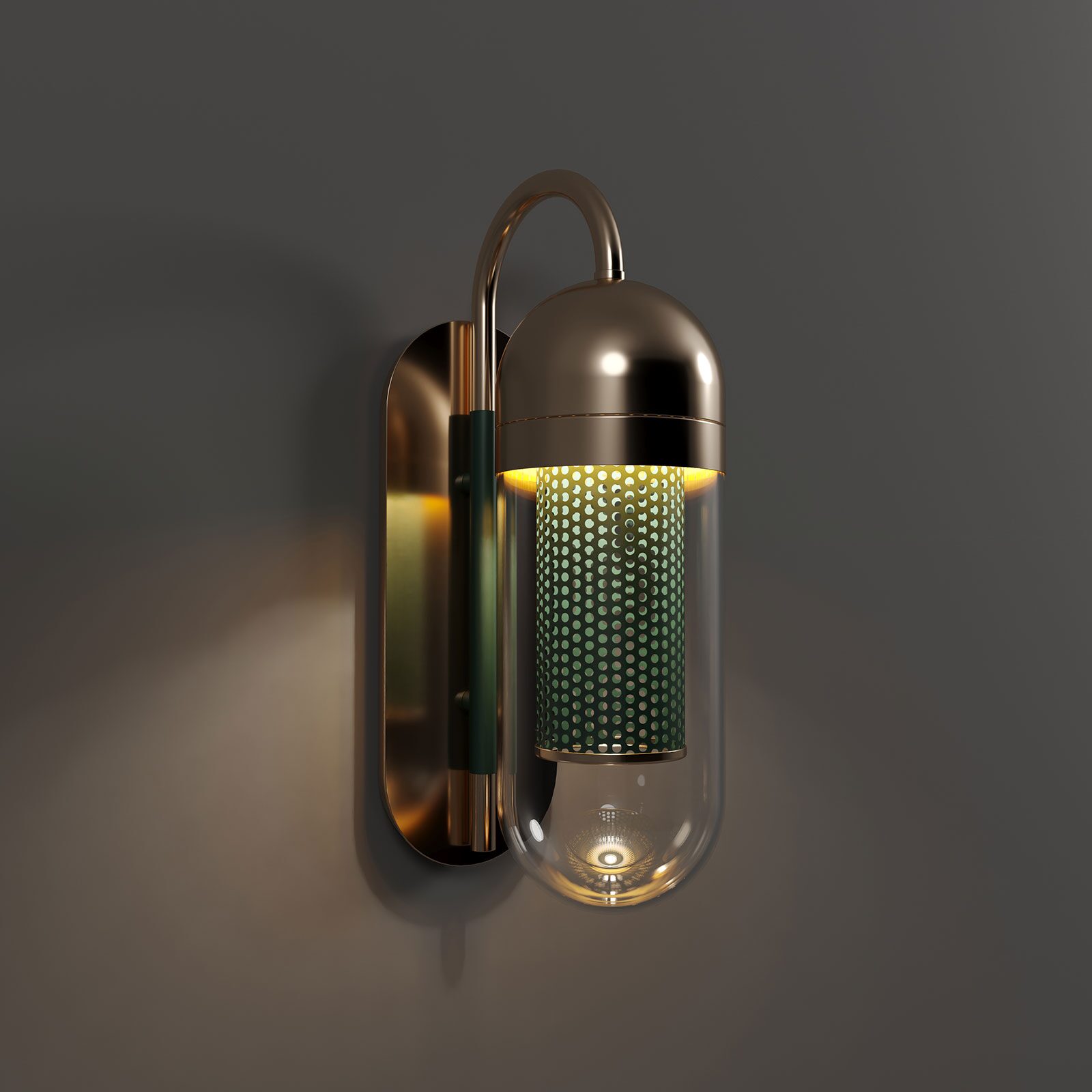 Denver Wall Lamp A luxury Denver Wall Lamp by Porus Studio, featuring a pill-shaped clear glass diffuser. The lamp is constructed with a curved polished brass arm and a mounting plate. Inside the glass, a lacquered green perforated stainless steel cylinder houses the light source, emitting a warm, diffused glow through the small circular cutouts. The lamp is mounted on a dark charcoal wall, casting a soft, atmospheric amber light.