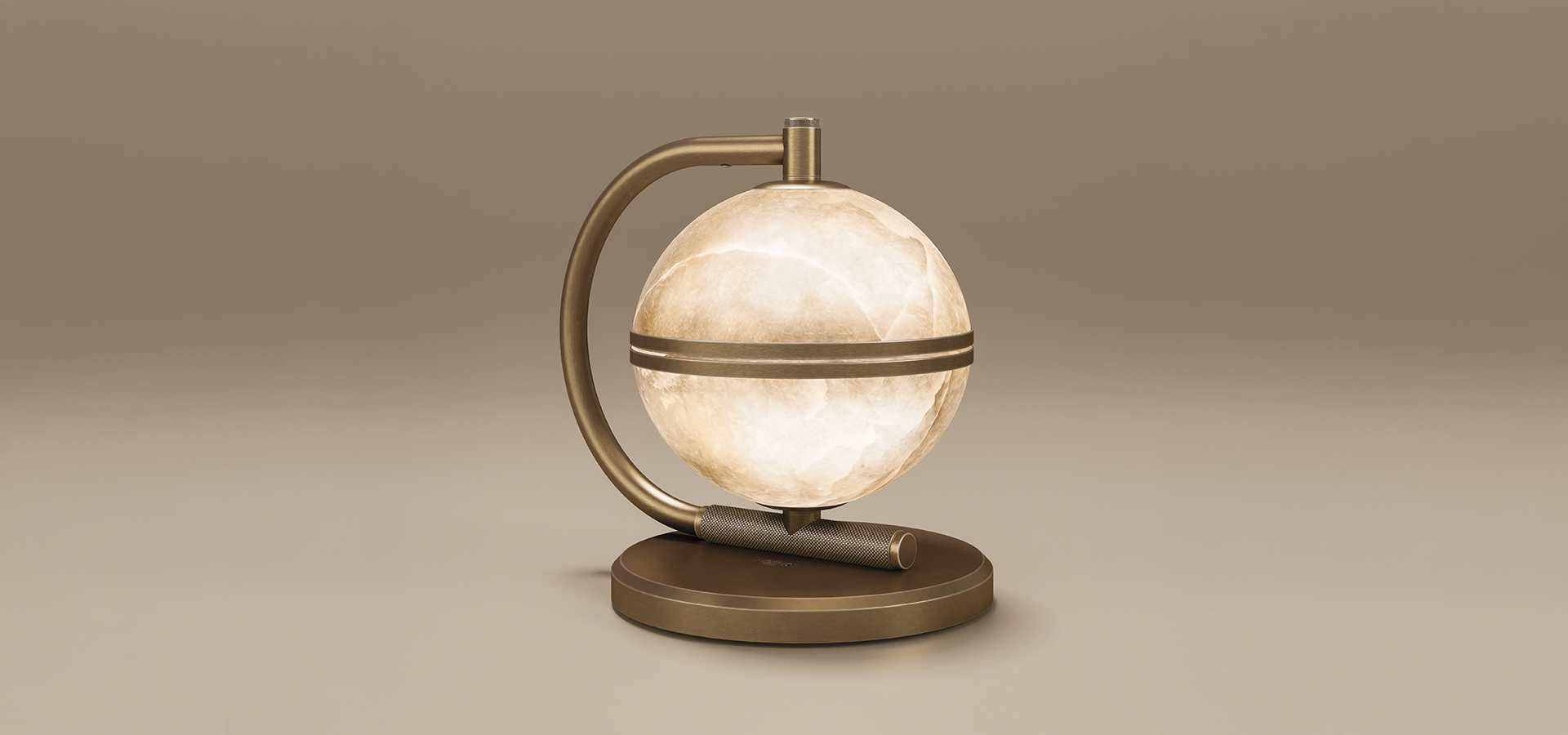 Oculus table lamp in aged brushed brass, its alabaster sphere lit from within and held by a curved brass arm above a round base with a knurled brass bar.
