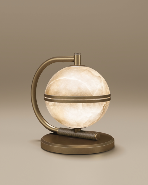 Oculus table lamp with an aged brushed brass structure and a spherical alabaster shade, shown glowing softly on a round brass base.