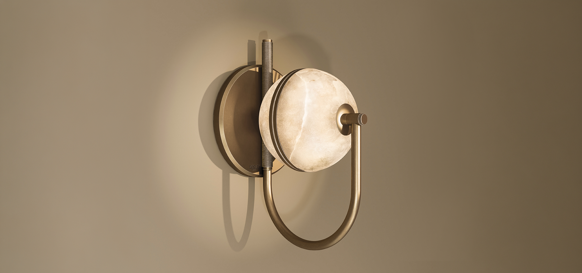 Wide view of the Oculus wall lamp with an illuminated alabaster disc, a knurled vertical rod and a curved aged brushed brass arm, glowing against a gradient taupe wall.